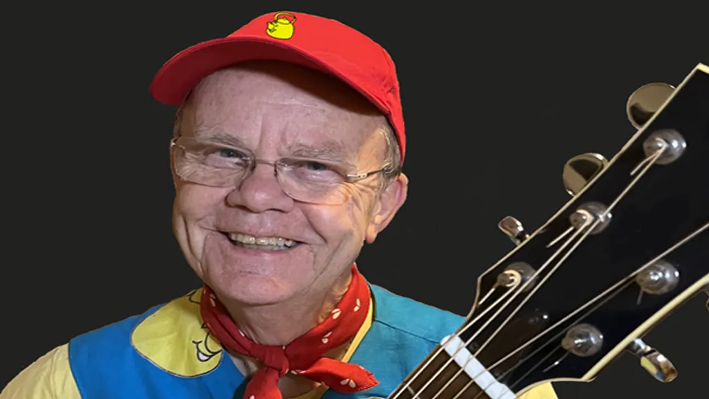 Smiling man in a colourful outfit holding a guitar