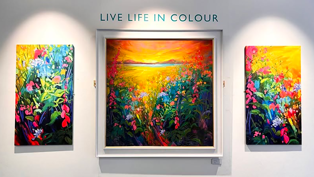 Two canvases and an art piece in a frame on the wall at the Harbour Arts Centre, the word 'Live Life In Colour' is also on the wall above the art